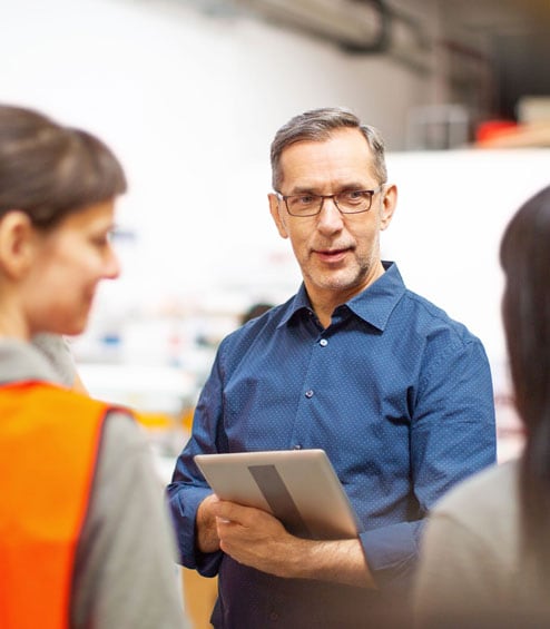 Older white man discussing with younger coworkers in factory setting