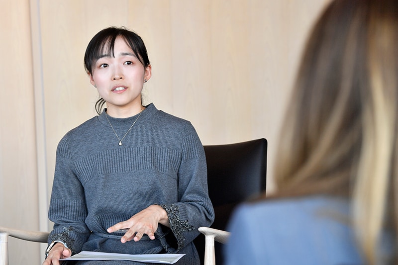 菅原 萌の写真。後ろで結んだ黒髪の日本人女性で、グレーのセーターを着ている。