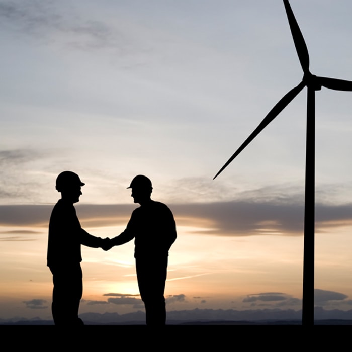 men shaking hands next to wind turbine