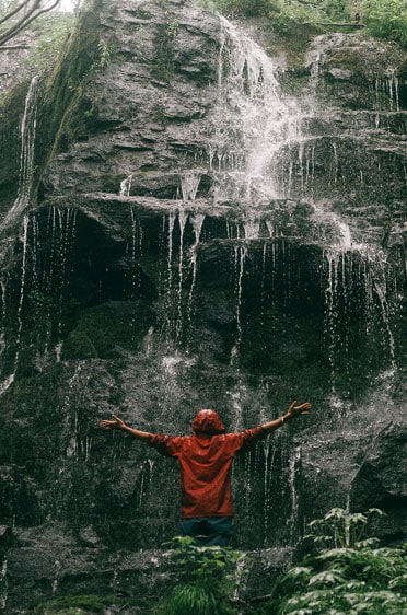 Man with arms outstretched at base of waterfall